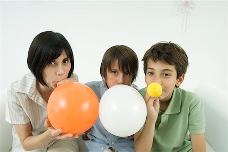 Mother and two sons inflating balloons, looking at camera Stock Photo - Premium Royalty-Free, Code: 695-03380675