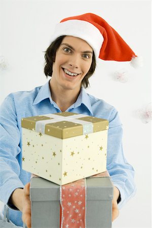 Young man wearing Santa hat, holding out Christmas gifts, smiling at camera Stock Photo - Premium Royalty-Free, Code: 695-03380673