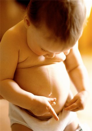 Baby in diaper, standing, looking down, with hands on belly, close-up Stock Photo - Premium Royalty-Free, Code: 695-03381142