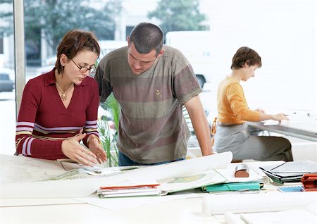 Woman and man looking at plans, woman sitting in background Stock Photo - Premium Royalty-Free, Code: 695-03381197