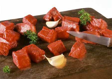 Cubed beef on cutting board with knife, cloves of garlic and sprigs of parsley, close-up Stock Photo - Premium Royalty-Free, Code: 695-03381295