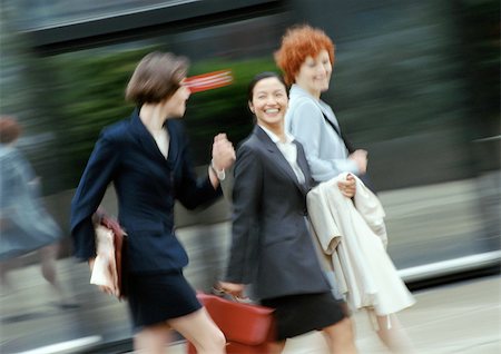 simsearch:695-05770005,k - Three businesswomen walking in street, smiling, blurred Fotografie stock - Premium Royalty-Free, Codice: 695-03381688
