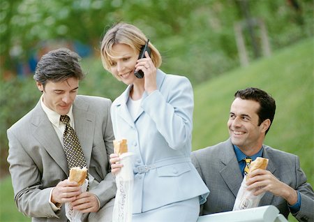 Three business people holding sandwiches outdoors, one using cell phone Stock Photo - Premium Royalty-Free, Code: 695-03381683