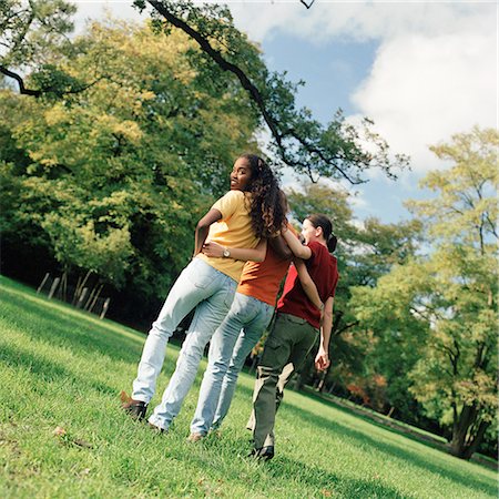 simsearch:633-05401680,k - Three young women walking on grass with arms around each other, rear view, one looking over shoulder Foto de stock - Sin royalties Premium, Código: 695-03382464