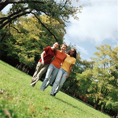 Three young women walking on grass with arms around each other, front view, full length Stock Photo - Premium Royalty-Free, Code: 695-03382465