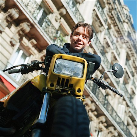 simsearch:695-03382568,k - Teenage boy on stationary motorcycle, smiling at camera, low angle view Fotografie stock - Premium Royalty-Free, Codice: 695-03382605