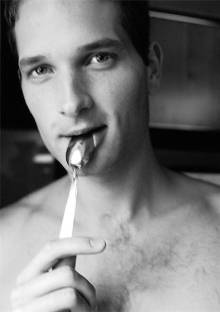 Barechested man holding spoon to lips, looking at camera, close-up, black and white. Stock Photo - Premium Royalty-Free, Code: 695-03382669