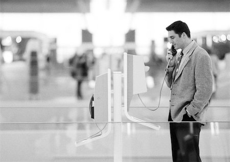 public talk - Businessman using pay phone in terminal, black and white. Stock Photo - Premium Royalty-Free, Code: 695-03382784