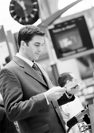 simsearch:696-03402790,k - Businessman standing in terminal, looking at tickets, black and white. Stock Photo - Premium Royalty-Free, Code: 695-03382819