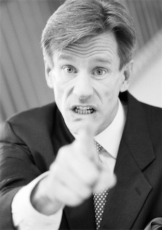 Businessman pointing at camera, hand blurred in foreground, black and white, portrait. Stock Photo - Premium Royalty-Free, Code: 695-03382813