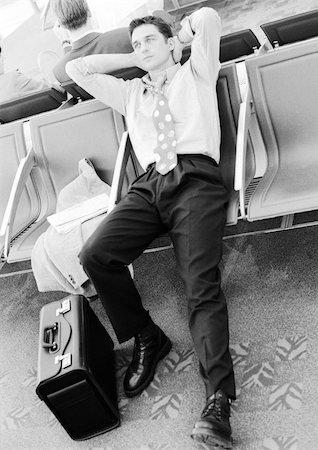simsearch:695-03382908,k - Businessman in airport lounge leaning back in seat, black and white. Fotografie stock - Premium Royalty-Free, Codice: 695-03382821