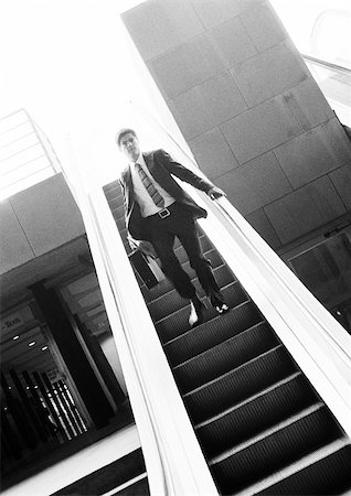 Businessman going down escalator, b&w. Stock Photo - Premium Royalty-Free, Code: 695-03382907