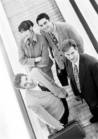 simsearch:695-03382908,k - Group of business people on moving walkway looking up at camera, high angle view, b&w. Fotografie stock - Premium Royalty-Free, Codice: 695-03382913