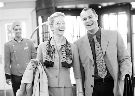 executive couple hotel - Businessman and businesswoman in hotel in front of bellhop, smiling at camera, b&w. Stock Photo - Premium Royalty-Free, Code: 695-03382938