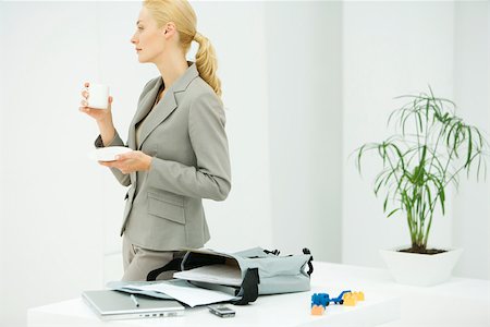 family tea - Professional woman holding coffee cup, looking away, bag with laptop and documents on table Stock Photo - Premium Royalty-Free, Code: 695-03390028