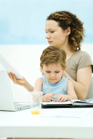 Mother holding son on lap, sitting in front of laptop, frowning at document Stock Photo - Premium Royalty-Free, Code: 695-03390033