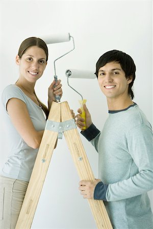 simsearch:695-03389240,k - Couple standing on ladder, both holding up paint rollers and smiling at camera Stock Photo - Premium Royalty-Free, Code: 695-03390055