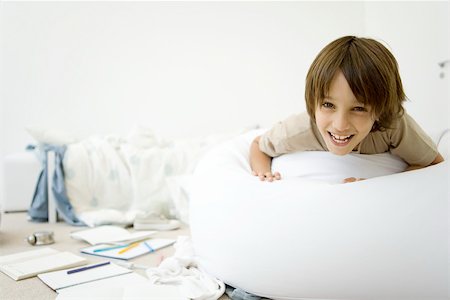 Boy lying on stomach in messy room, smiling at camera Stock Photo - Premium Royalty-Free, Code: 695-03390085