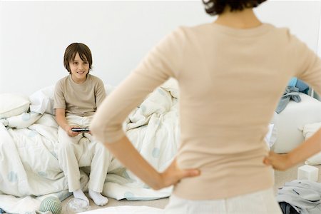 scolding - Boy playing handheld video game in messy bedroom, mother standing in foreground with hands on hips Stock Photo - Premium Royalty-Free, Code: 695-03390088