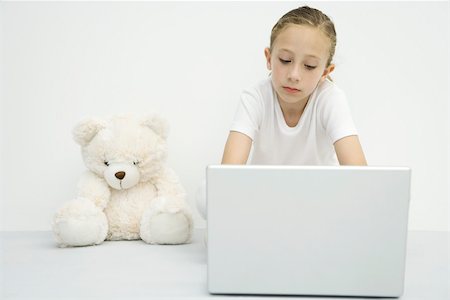 people sitting alone girl with teddy bear - Girl sitting beside teddy bear, using laptop computer Stock Photo - Premium Royalty-Free, Code: 695-03390095