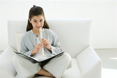 Girl sitting cross-legged on armchair, playing recorder Stock Photo - Premium Royalty-Free, Code: 695-03390093