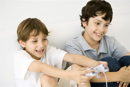 simsearch:6108-07969509,k - Two boys playing video game together, one holding controller, both smiling Stock Photo - Premium Royalty-Free, Code: 695-03390105