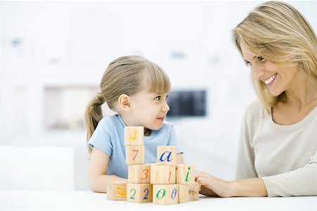 Mother and daughter sitting with blocks, smiling at each other Stock Photo - Premium Royalty-Free, Code: 695-03390247