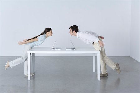 simsearch:614-01821282,k - Man and woman at opposite ends of table, leaning towards each other, laptop computers between them Stock Photo - Premium Royalty-Free, Code: 695-03390277