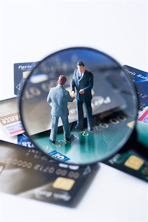 figurines businessman - Miniature businessmen shaking hands on pile of credit cards, viewed through magnifying glass Stock Photo - Premium Royalty-Free, Code: 695-03390407