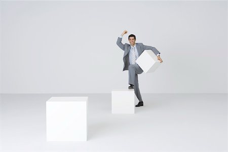 Homme d'affaires transportant des blocs, sauter sur le bloc plus grand Photographie de stock - Premium Libres de Droits, Code: 695-03390544