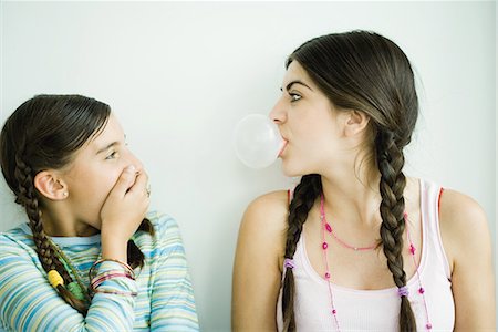 Two young female friends, one blowing bubble while other watches and covers mouth Stock Photo - Premium Royalty-Free, Code: 696-03394054