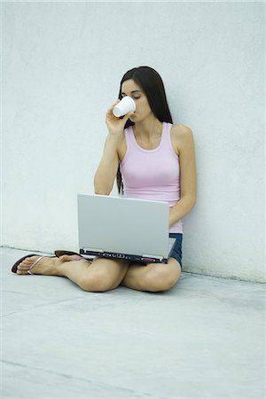 simsearch:696-03394188,k - Woman sitting on ground, using laptop and drinking from disposable cup, full length Fotografie stock - Premium Royalty-Free, Codice: 696-03394119