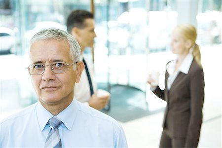 simsearch:632-03630033,k - Mature businessman looking at camera, portrait, associates in background Stock Photo - Premium Royalty-Free, Code: 696-03394306