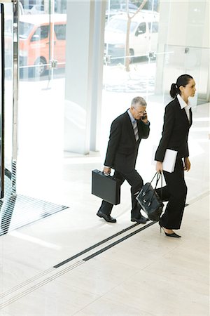 Business associates walking in lobby, one using cell phone, full length Stock Photo - Premium Royalty-Free, Code: 696-03394301