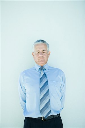 Mature businessman standing, hands behind back, eyes closed Stock Photo - Premium Royalty-Free, Code: 696-03394329