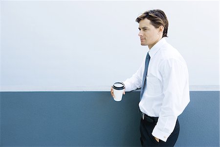 simsearch:695-05766182,k - Young businessman standing, holding hot beverage, hand in pocket Fotografie stock - Premium Royalty-Free, Codice: 696-03394321