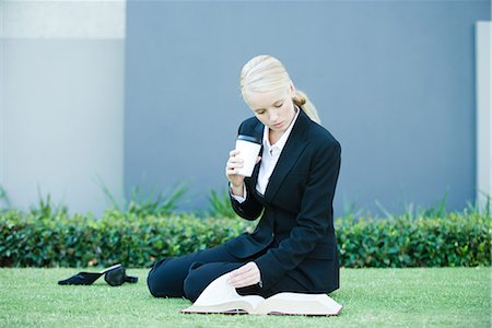 simsearch:632-01271843,k - Young businesswoman sitting on the ground outdoors, reading book, holding hot beverage Stock Photo - Premium Royalty-Free, Code: 696-03394345