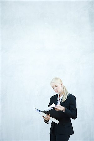 simsearch:632-01271843,k - Young businesswoman standing, looking at file, three quarter length Stock Photo - Premium Royalty-Free, Code: 696-03394348