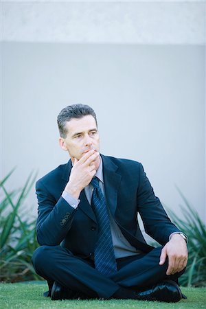 simsearch:695-03373745,k - Businessman sitting on the ground outdoors, looking away, finger on lips Foto de stock - Royalty Free Premium, Número: 696-03394343