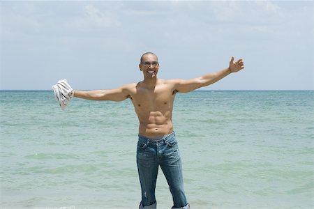 Man standing by the sea with arms outstretched, holding shirt in hand, smiling Stock Photo - Premium Royalty-Free, Code: 696-03395234