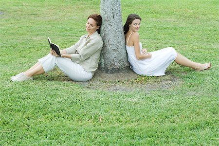simsearch:696-03402697,k - Mother and daughter leaning against tree trunk, woman reading book, teen girl smiling at camera Foto de stock - Sin royalties Premium, Código: 696-03395262