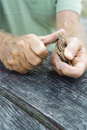 Man whittling piece of bark, cropped view of hands Stock Photo - Premium Royalty-Free, Code: 696-03395419