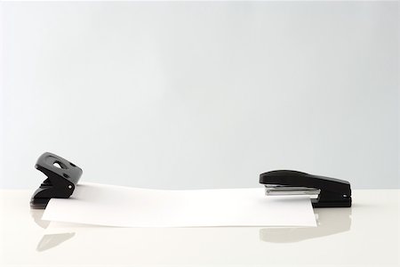 Sheet of paper, resting in hole puncher on one end and stapler on the other Foto de stock - Sin royalties Premium, Código: 696-03396034