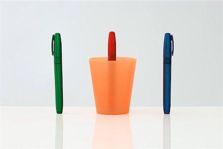 Pens standing upright in a row, the middle pen upside down inside of cup Stock Photo - Premium Royalty-Free, Code: 696-03396031