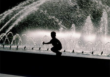 Silhouette of boy crouching on edge of fountain Stock Photo - Premium Royalty-Free, Code: 696-03396823