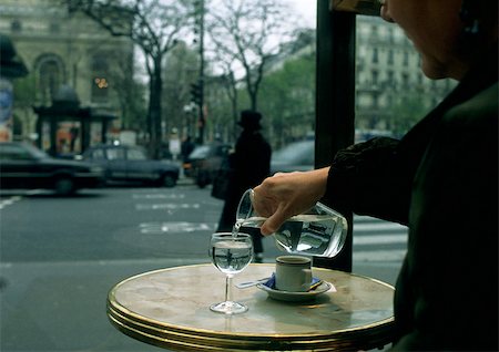 Person sitting at table on cafe terrace, pouring water from carafe Foto de stock - Sin royalties Premium, Código: 696-03396847