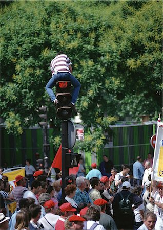 semaforo rosso - Man sitting on traffic light post in middle of crowd Fotografie stock - Premium Royalty-Free, Codice: 696-03397020
