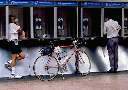 NY, NY, two men using pay phones, one with bike Stock Photo - Premium Royalty-Free, Code: 696-03397062