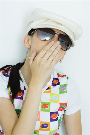 Teen girl wearing cap and sunglasses, covering mouth, portrait Stock Photo - Premium Royalty-Free, Code: 696-03393950