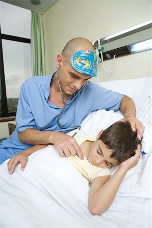 simsearch:400-04657502,k - Boy lying in hospital bed, sleeping, doctor holding stethoscope to boy's chest Stock Photo - Premium Royalty-Free, Code: 696-03393974